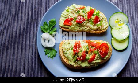 Due toast di pane biologico con avocado e pomodori ciliegini. Foto Stock