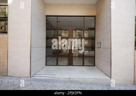 Portale stradale esterno di un edificio residenziale con pavimento in marmo crema e piastrelle e una doppia porta in metallo Foto Stock