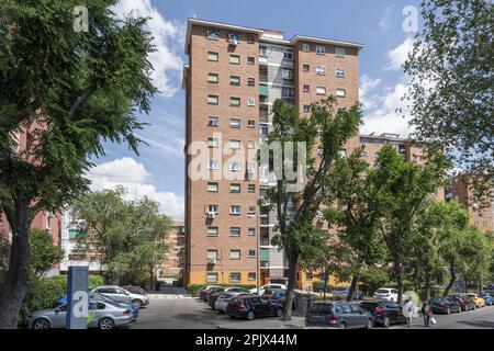 Facciata di un edificio di appartamenti con alcune nuvole in un cielo di sorgente blu e con graziosi alberi frondosi sulla strada Foto Stock