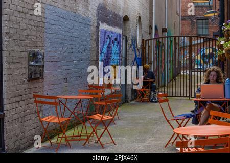 Knoxville, Tennessee, USA - 25 marzo 2023: Pubblico all'aperto seduto in un vicolo con murale dipinto su pareti in mattoni e invitanti sedie in metallo arancione AN Foto Stock