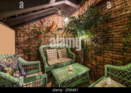 Un corridoio di nightclub decorato in stile spiaggia con sabbia sul pavimento e un salotto di vimini colorato di verde con tavolo da caffe' abbinato Foto Stock