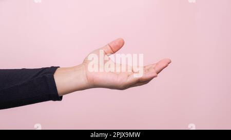 Primo piano della mano della donna che raggiunge pronto per aiutare o ricevere, isolato su sfondo rosa. Aiutare la mano tesa per la salvezza. Foto Stock