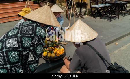 Venditori vietnamiti di frutta che indossano un cappello a cono Foto Stock