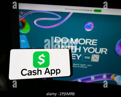 Persona che tiene in mano uno smartphone con il logo della società fintech statunitense Cash App Investing LLC sullo schermo di fronte al sito Web. Messa a fuoco sul display del telefono. Foto Stock