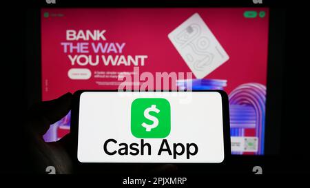 Persona che tiene il cellulare con il logo della società fintech US Cash App Investing LLC sullo schermo di fronte al sito web aziendale. Messa a fuoco sul display del telefono. Foto Stock