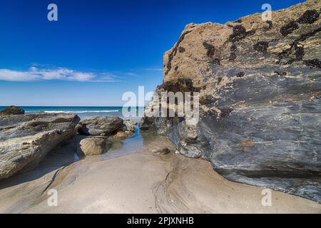 Vista bassa marea - Rocks a vista, piscina rocciosa, spiaggia sabbiosa e vista sul mare a Portreath Beach, Cornovaglia, con cielo blu all'inizio dell'estate. Foto Stock