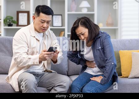 Famiglia coppia uomo e donna seduta sul divano a casa asiatico famiglia uomo cercando di chiamare il medico per moglie malata. Foto Stock