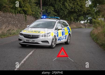 Winsley, Wiltshire, Regno Unito, settembre 25 2022, una macchina della polizia parcheggiata obliquamente nel mezzo di una strada di campagna con un triangolo di avvertimento fiorente dentro Foto Stock