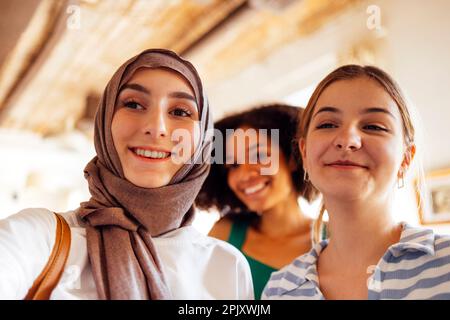 Primo piano ritratti di tre ragazze adolescenti sorridenti. Musulmano in un hijab, afro americano e femmine bianche adolescenti. Ragazze giovani e positive indoor. Venerdì Foto Stock