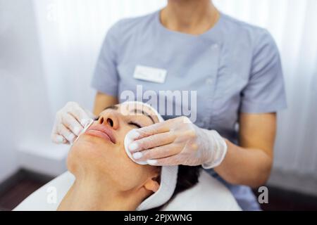 Primo piano di bella giovane donna brunetta durante la pulizia del viso e il massaggio. Procedure cosmetiche in un salone di bellezza o in una clinica. Candele accese su ba Foto Stock