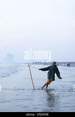 karachi pakistan 2021, un pescatore che tira la rete di pesca per catturare i pesci, alla vista del mare in ora di sera. Foto Stock