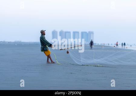 karachi pakistan 2021, un pescatore che tira la rete di pesca per catturare i pesci, alla vista del mare in ora di sera. Foto Stock