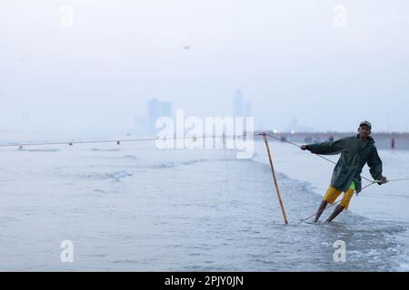 karachi pakistan 2021, un pescatore che tira la rete di pesca per catturare i pesci, alla vista del mare in ora di sera. Foto Stock