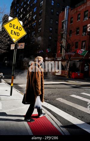 Donna che indossa una maschera facciale e un cappotto di pelliccia che attraversa una strada a New York City Foto Stock