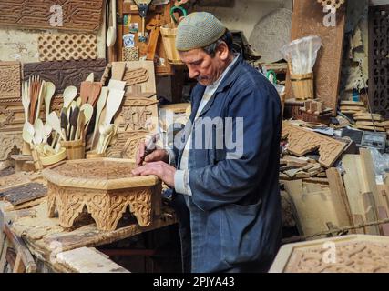 Fez, Marocco - 07 gennaio 2020: Uomo sconosciuto nella sua lavorazione del legno o scultura officina vicino al mercato di strada. molti souvenir di legno e prodotti intorno a lui Foto Stock