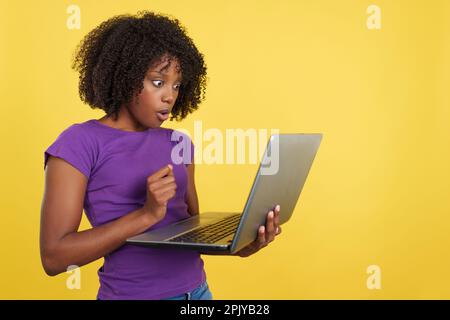 Donna con capelli afro che guarda un notebook con espressione scioccata Foto Stock