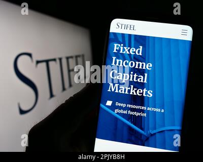 Persona in possesso di smartphone con pagina web della società di investimento statunitense Stifel Financial Corp. Sullo schermo con logo. Messa a fuoco al centro del display del telefono. Foto Stock