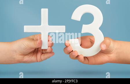 Più tre. Il limite di età è di 3 anni. Numero bianco 3 più in mano su uno sfondo blu primo piano. Aggiungere tre concetti. Foto Stock