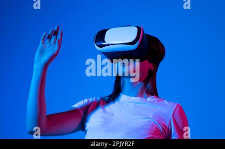 Bruna donna in realtà virtuale cuffie per giocare a videogiochi con un amico e gesturing con le mani. Concetto di gioco del futuro. Foto Stock