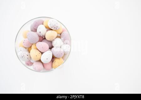 Mini uova al cioccolato rosa, giallo, bianco e viola in un recipiente di vetro su sfondo bianco (Pasqua) Foto Stock