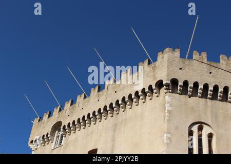 Facciata in pietra di una parte di Château Grimaldi nella piazza Haut de Cagnes su un cielo blu chiaro pomeriggio con pali di bandiera vuoti (Cagnes sur Mer, Francia) Foto Stock