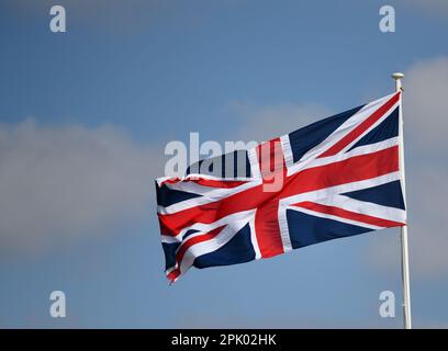 Una bandiera dell'Unione, nota anche come Union Jack, che frulica al vento contro un cielo blu con alcune nuvole bianche Foto Stock