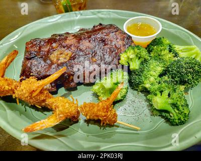 Costolette di maiale alla griglia e gamberi di cocco con broccoli freschi su un piatto verde Foto Stock
