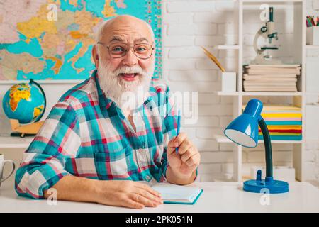 Insegnante felice e maturo seduto in classe. Insegnante allegro che ama il suo lavoro. Vecchio professore divertente. Insegnante sorridente. Foto Stock