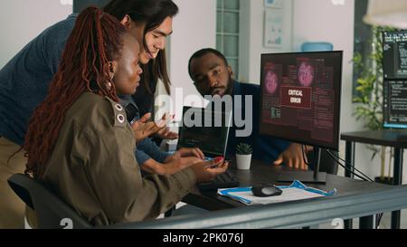 Gruppo multietnico di ingegneri IT che si occupano dell'avviso di hacking, visualizzando l'errore del server di sicurezza sul computer. Sviluppatori di software che hanno violato computer e sistema, lavorando su database. Foto Stock