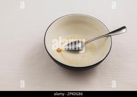 Ciotola di cereali quasi vuota con cucchiaio su fondo bianco testurizzato. Foto Stock