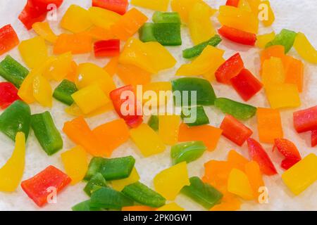 Capsicum annuum crudo a dadini, rosso, giallo, arancione e verde - peperoni sulla parte superiore di carta bianca. Foto Stock