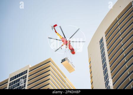 Hallandale Beach, Miami, Florida - 4 aprile 2023: Elicottero che solleva l'enorme Air-Condition Roof Top Centrale unità al tetto della cima del alto edificio Foto Stock