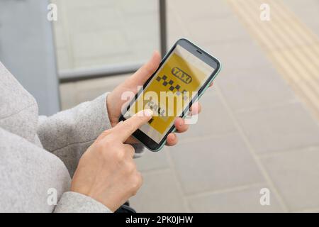 Donna che ordina un taxi con app sul suo smartphone all'aperto, closeup Foto Stock