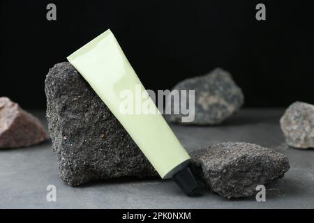 Tubo di crema per le mani tra le pietre su un tavolo grigio su sfondo scuro. Modello per il design Foto Stock