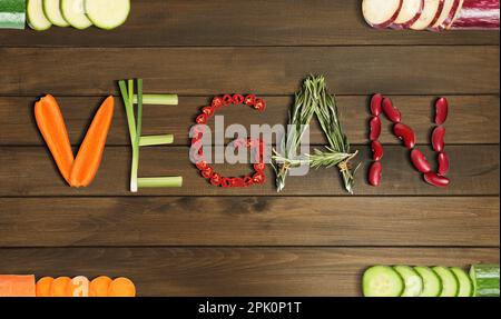 Parola VEGAN fatto di diverse verdure fresche gustose su sfondo di legno, piatto Foto Stock