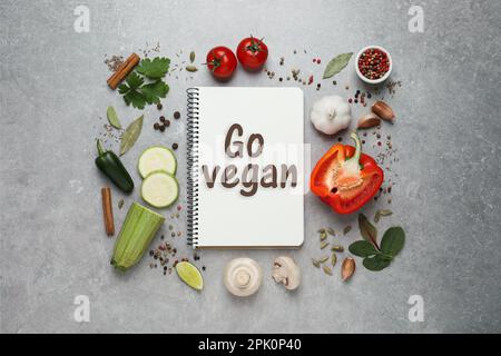 Notebook con frase Go Vegan, verdure fresche e spezie su sfondo grigio chiaro, piatto Foto Stock