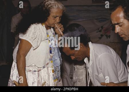 I membri del culto religioso afro-brasiliano Tambor de Mina si impegnarono in una cerimonia di guarigione (pagelanza) derivata dallo sciamanesimo amerindo. Il Mãe de Santo sta soffiando fumo di sigaro sulla testa di un paziente. Foto Stock