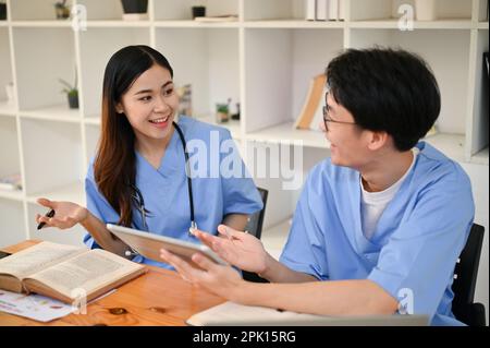 Due giovani studenti di medicina asiatici stanno discutendo i loro casi medici e si stanno preparando per gli esami in una biblioteca insieme. Foto Stock