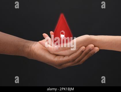 Persone che tengono goccia rossa in mani su sfondo scuro, primo piano. Concetto di donazione di sangue Foto Stock