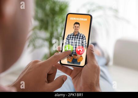 Uomo con smartphone che chiama un addetto all'assistenza professionale in interni, primo piano Foto Stock