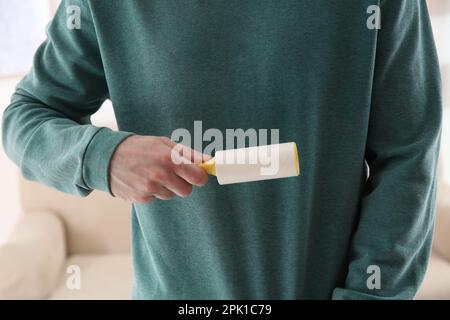 Uomo che pulisce la felpa verde con rullo per pelucchi su sfondo chiaro, primo piano Foto Stock