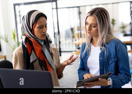 Occupate e diverse donne d'affari occasionali che discutono di lavoro e utilizzano il laptop in un ufficio moderno Foto Stock