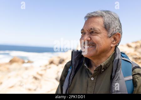 Felice uomo biraciale anziano che indossa zaino, escursioni in montagna Foto Stock