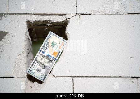 Una fattura del cento dollari si trova in un foro passante in un muro di mattoni di calcestruzzo aerato primo piano. Taglio di una porta in una parete di blocco di gas. Compensazione per co Foto Stock