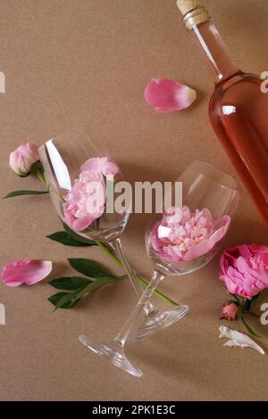 Bottiglia di vino rosato, bicchieri e belle peonie rosa su sfondo marrone, piatto Foto Stock