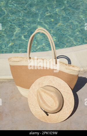 Elegante borsa e cappello vicino alla piscina all'aperto nelle giornate di sole. Accessori da spiaggia Foto Stock