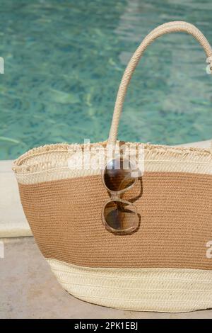 Borsa elegante e occhiali da sole vicino alla piscina all'aperto nelle giornate di sole. Accessori da spiaggia Foto Stock