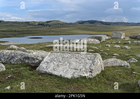 Novakovići, Žabljak, Montenegro – Agosto 2022: Stećak sul cimitero medievale „Grčko groblje“ e Riblje jezero (lago). Cimitero è iscritto sul Worl Foto Stock