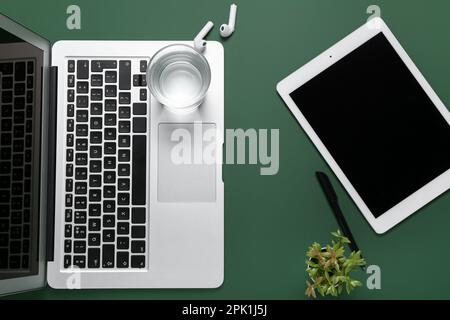 Composizione con notebook, tablet e auricolari su sfondo verde Foto Stock