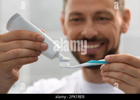 Uomo che applica dentifricio su pennello su sfondo sfocato, mettere a fuoco sulle mani Foto Stock